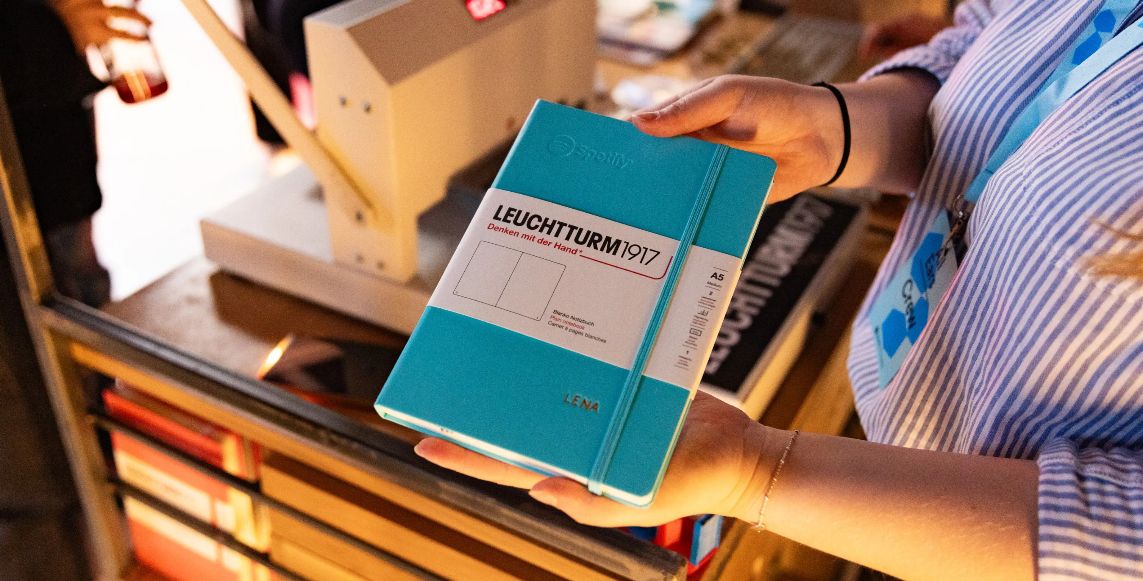 Individualisiertes Leuchtturm1917 Notizbuch mit Namensprägung. Libreta LEUCHTTURM1917 turquesa con grabado del nombre «LENA» en manos.